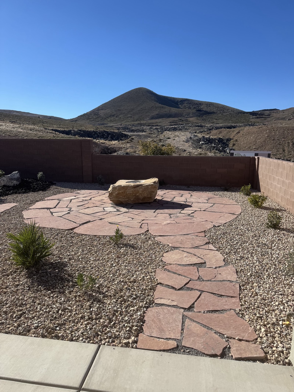 Flagstone fire-pit circle and desert landscaping beneath a red-rock peak